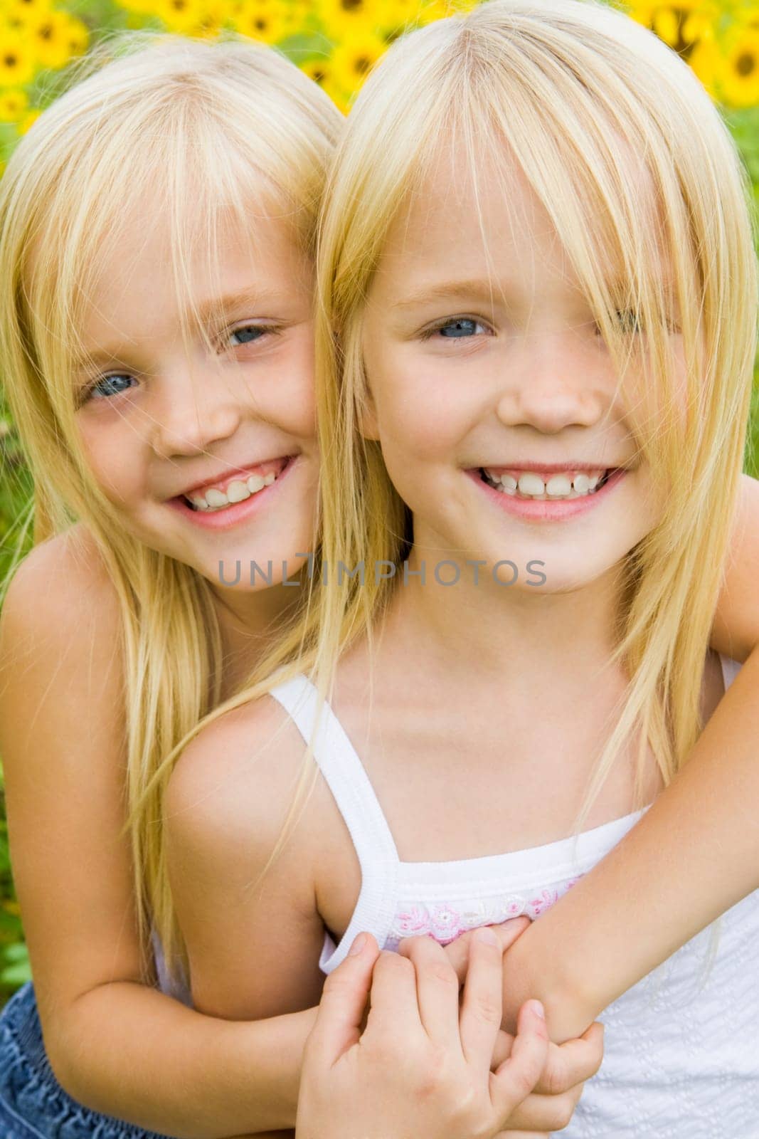 Portrait of cute girl embracing her twin sister and both looking at camera with smiles