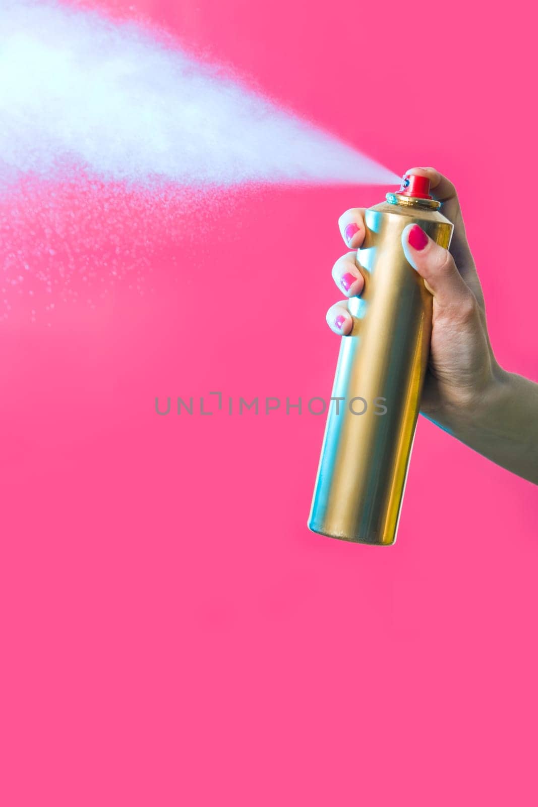 Photo of hair lacquer in females hand spraying it over red background