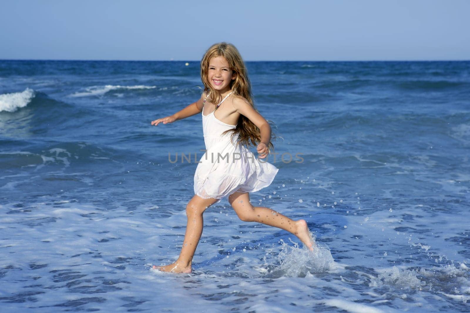 Little girl running beach shore splashing water in blue sea
