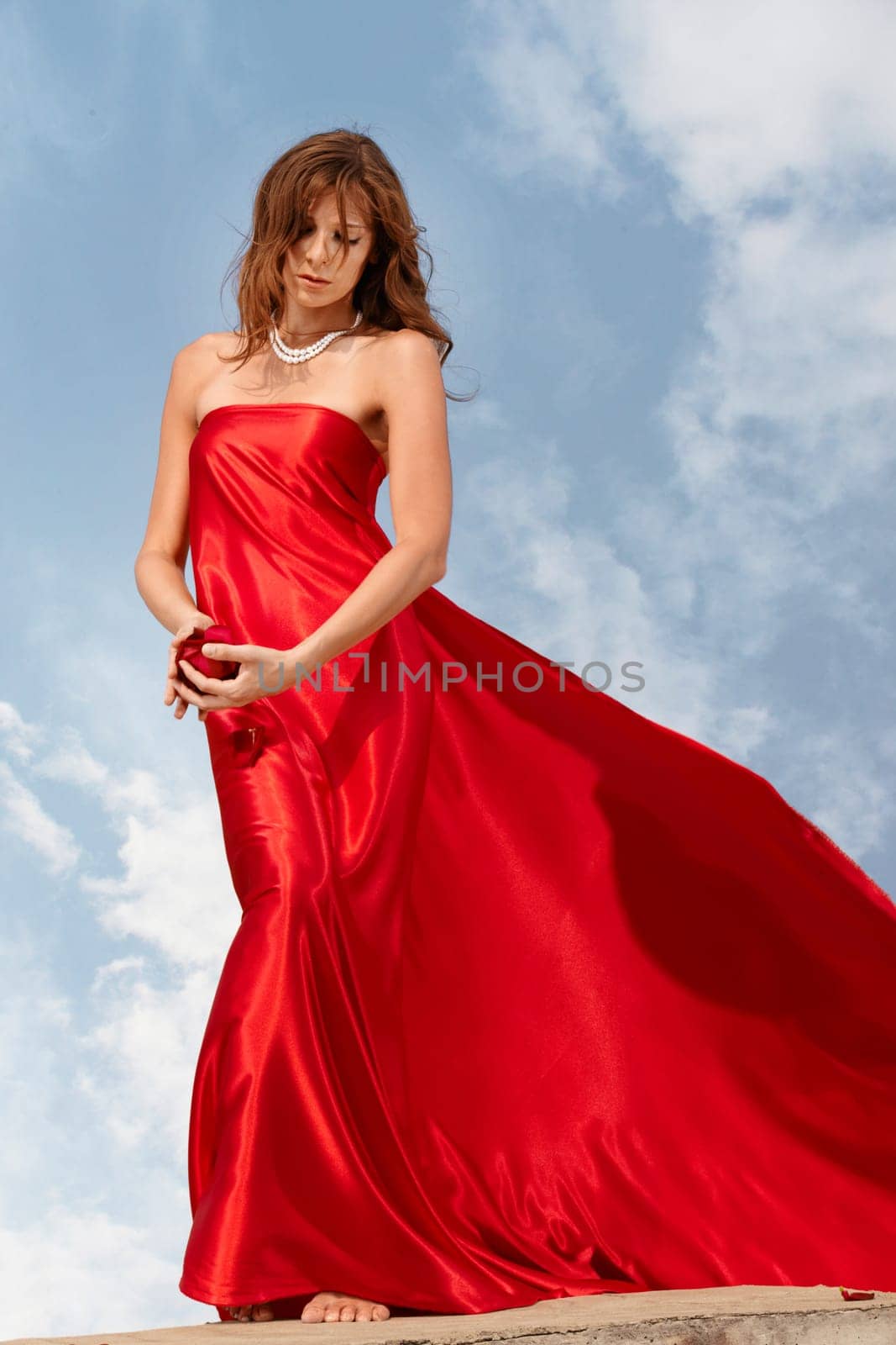 Photo of graceful female folded in bright red silk shawl looking at rosebud in her hands