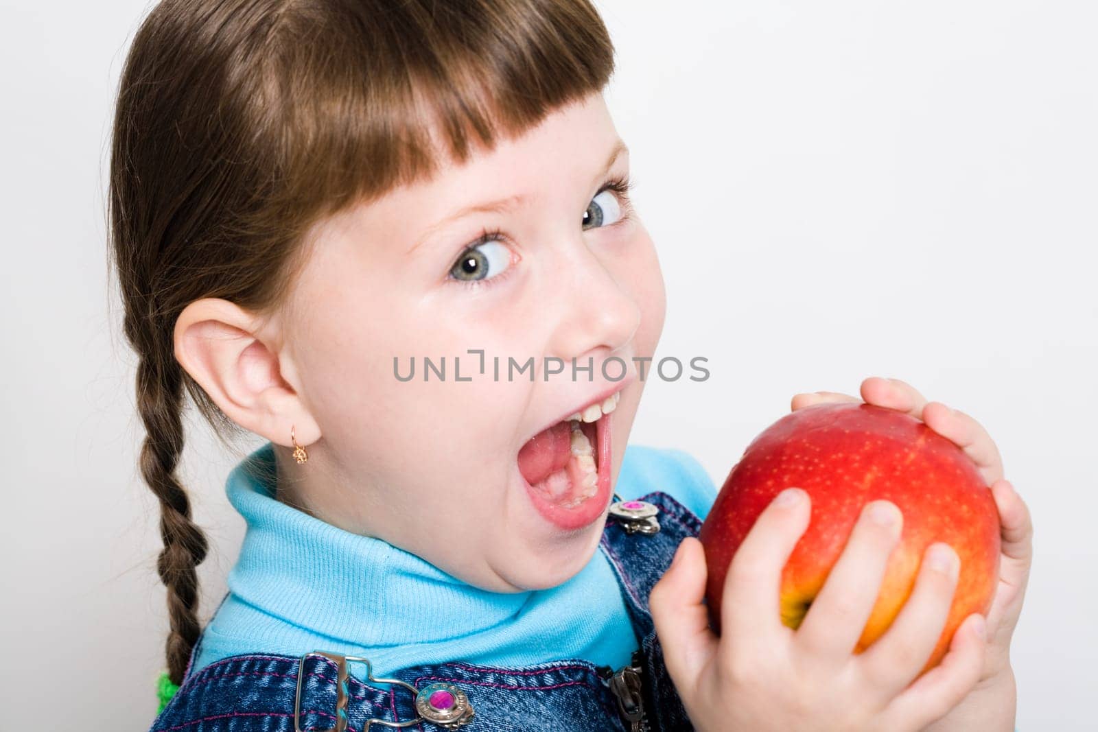 Cute girl looking aside with widely open mouth ready to eat red juicy apple