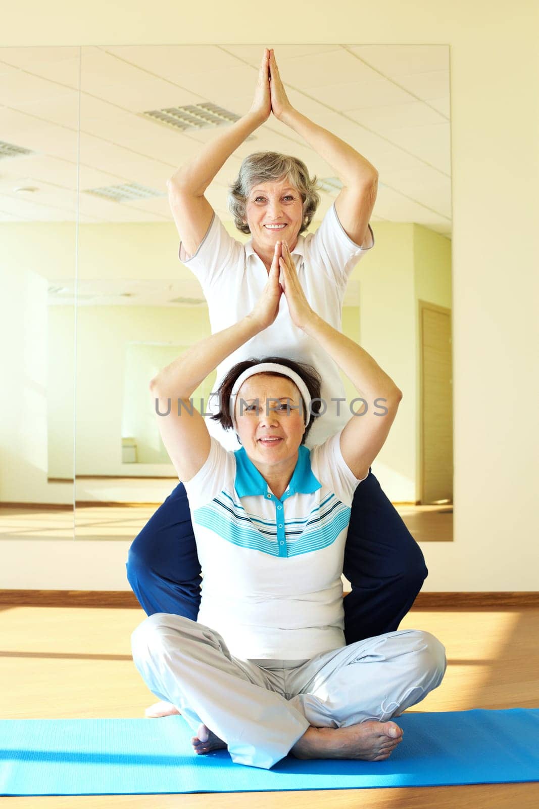Portrait of two aged females doing yoga exercise in sport gym