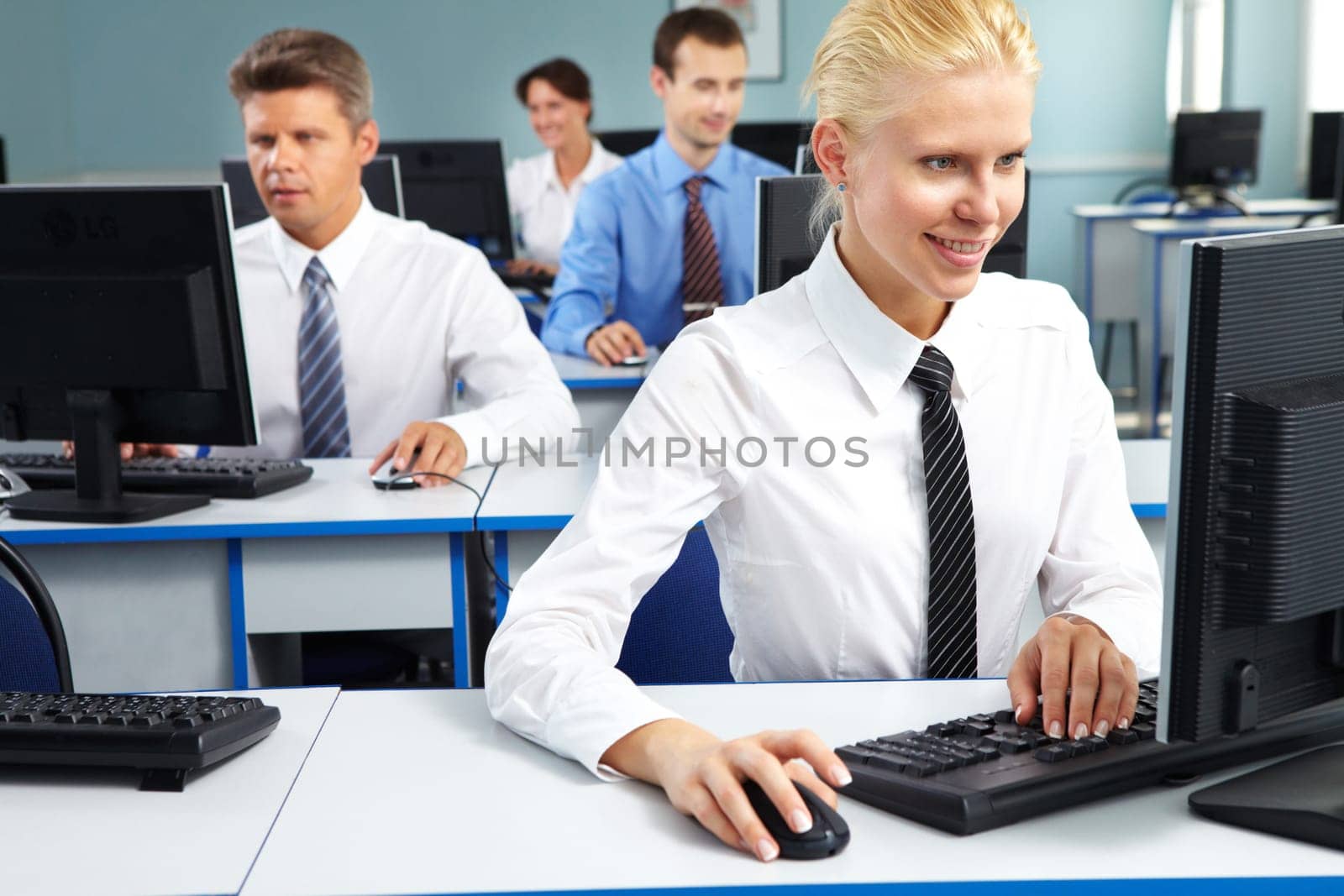 Young office worker sitting at computer and working among her colleagues