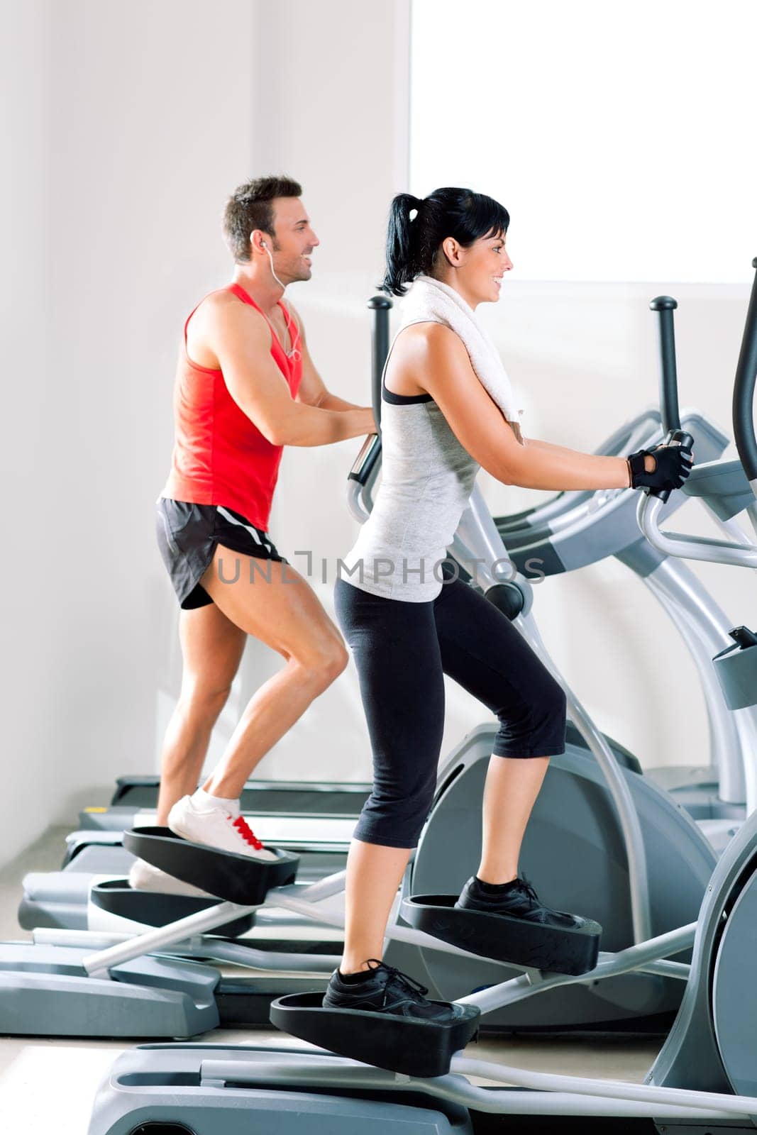 man and woman with elliptical cross trainer in sport fitness gym club