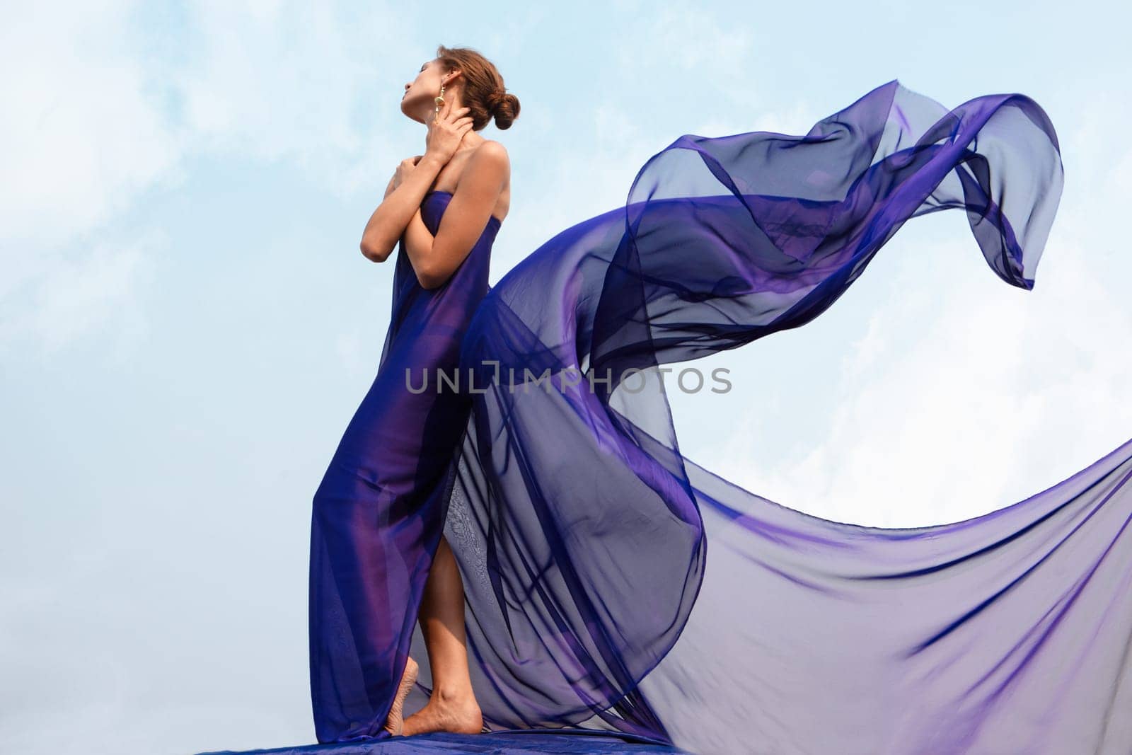 Photo of graceful female folded in dark blue chiffon shawl with cloudy sky at background
