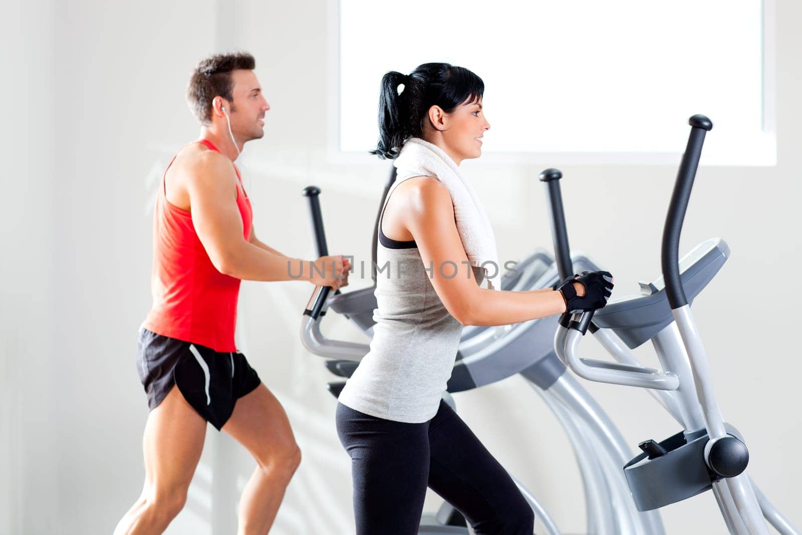 man and woman with elliptical cross trainer in sport fitness gym club