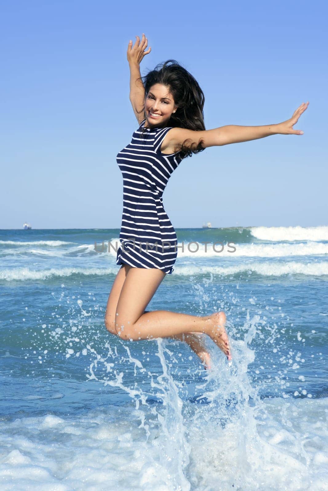 Beautiful summer brunette girl jumping on the blue beach
