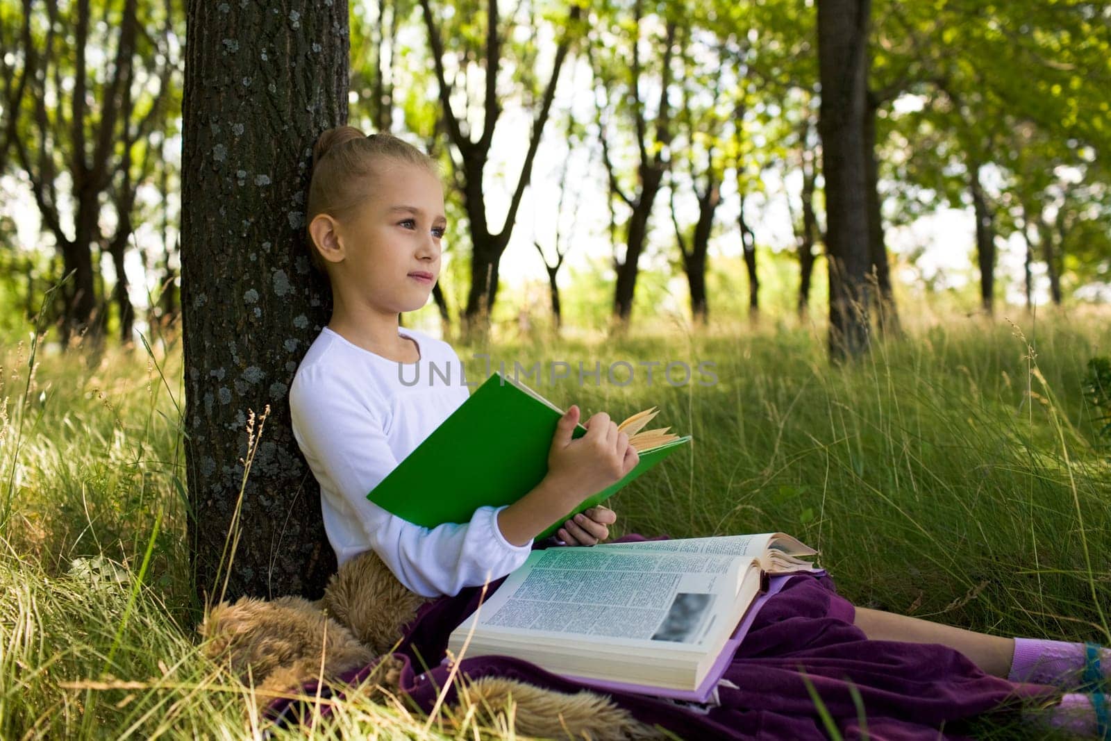 Pretty girl sitting under tree and thinking about something while reading books