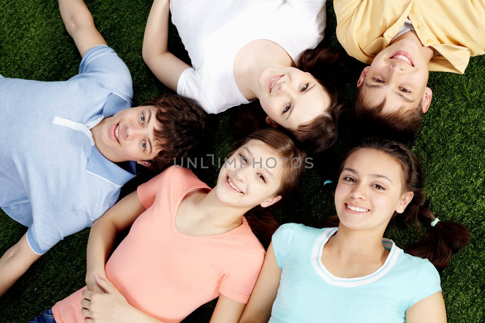 High angle view of five happy teens lying on grass