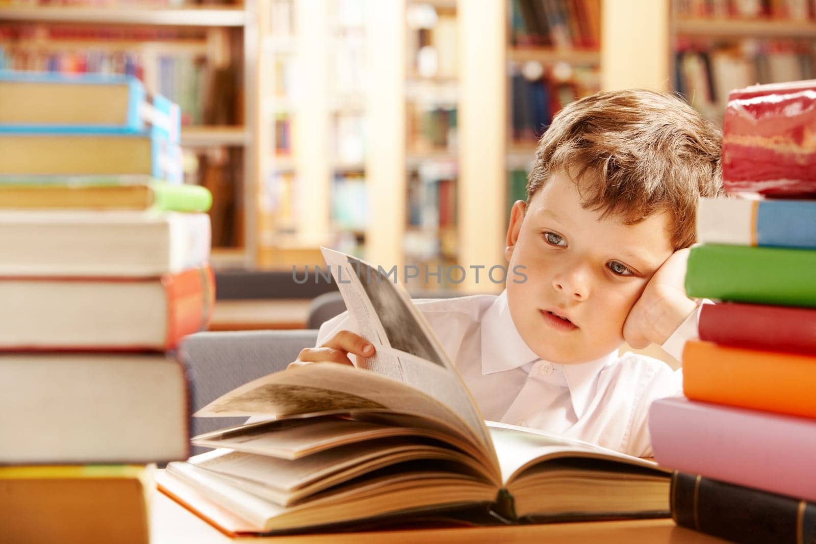 A schoolboy sitting in the library and turning the pages over