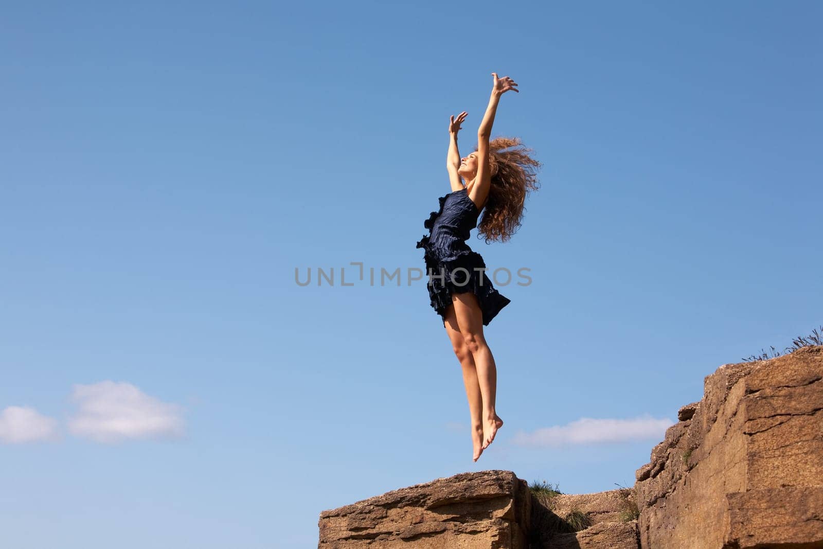 Photo of delighted female leaping over rocky cliff in excitement