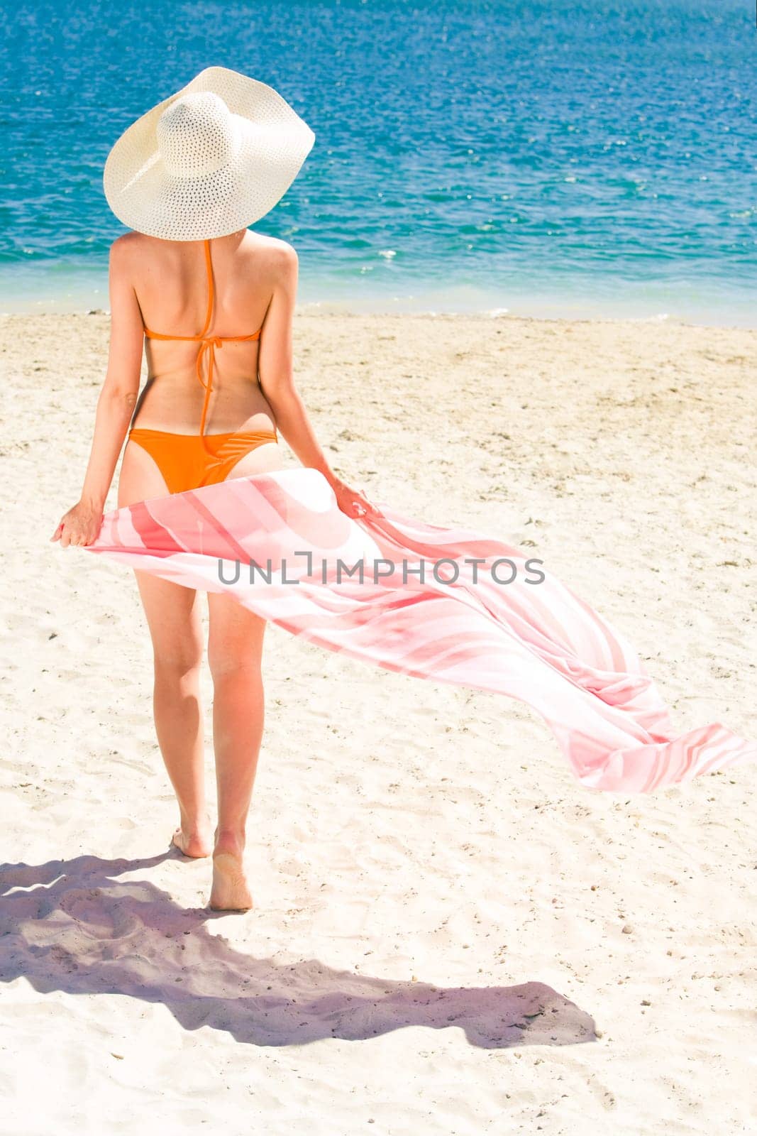 Portrait of woman with pareo walking aback along sandy beach during vacation