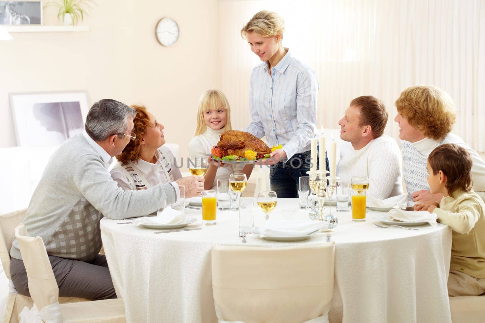 Portrait of big family sitting at festive table and looking at pretty woman with roasted turkey