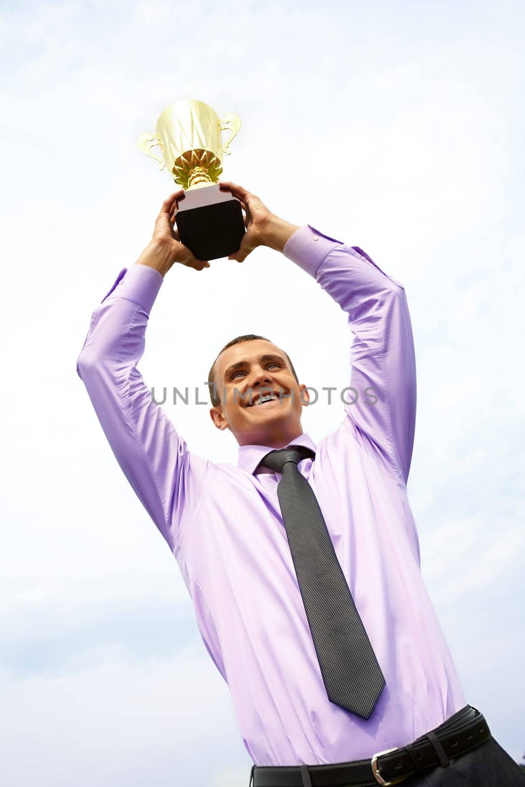 Portrait of happy businessman raising championship cup with cloudy sky above him