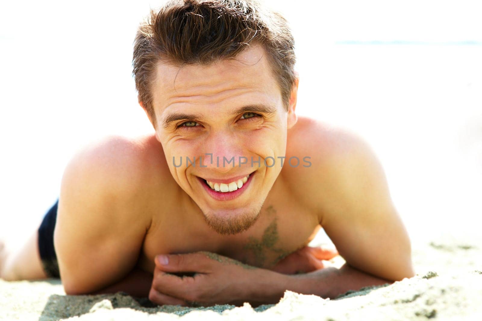 Photo of smiling guy lying on beach and looking at camera while sunbathing