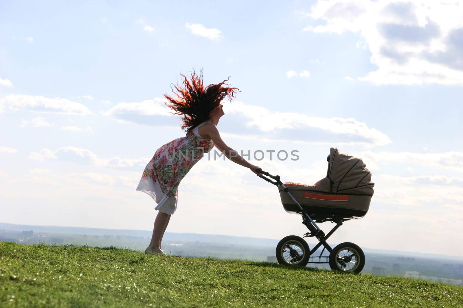 Emotional woman standing on green grassland and having fun while holding pram with baby