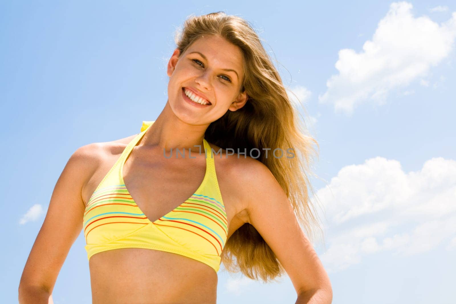 Portrait of happy woman in a yellow bikini on a background of sky