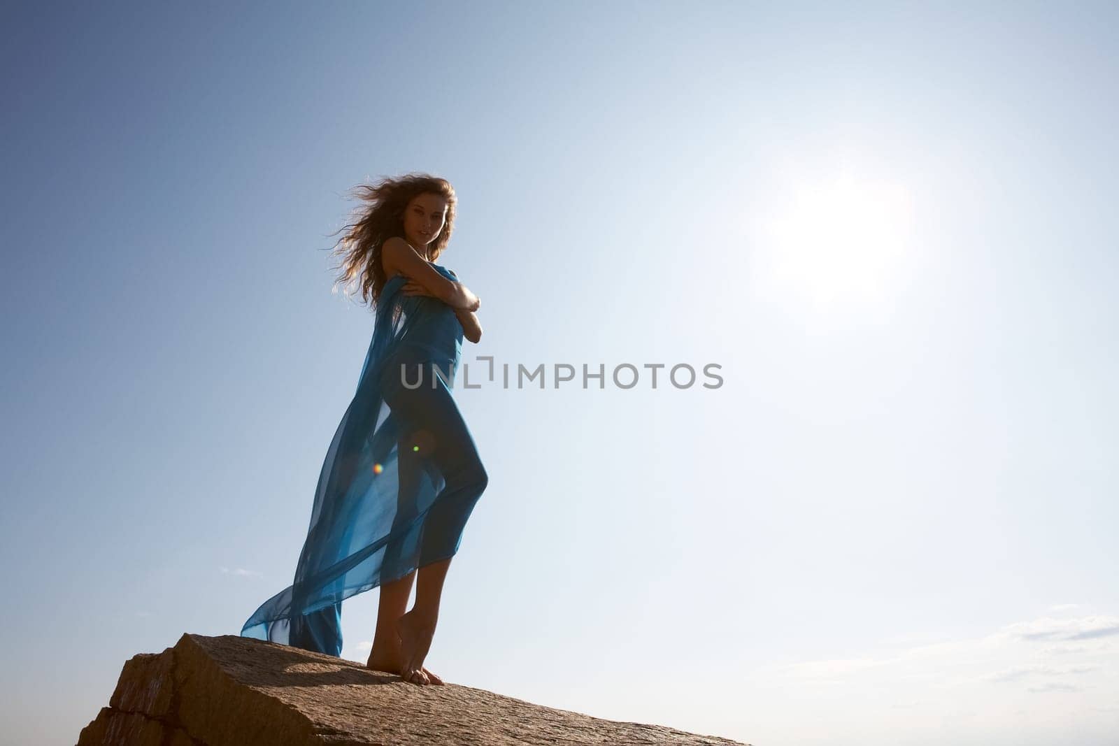 Photo of graceful female folded in dark blue chiffon shawl with sun shining at background