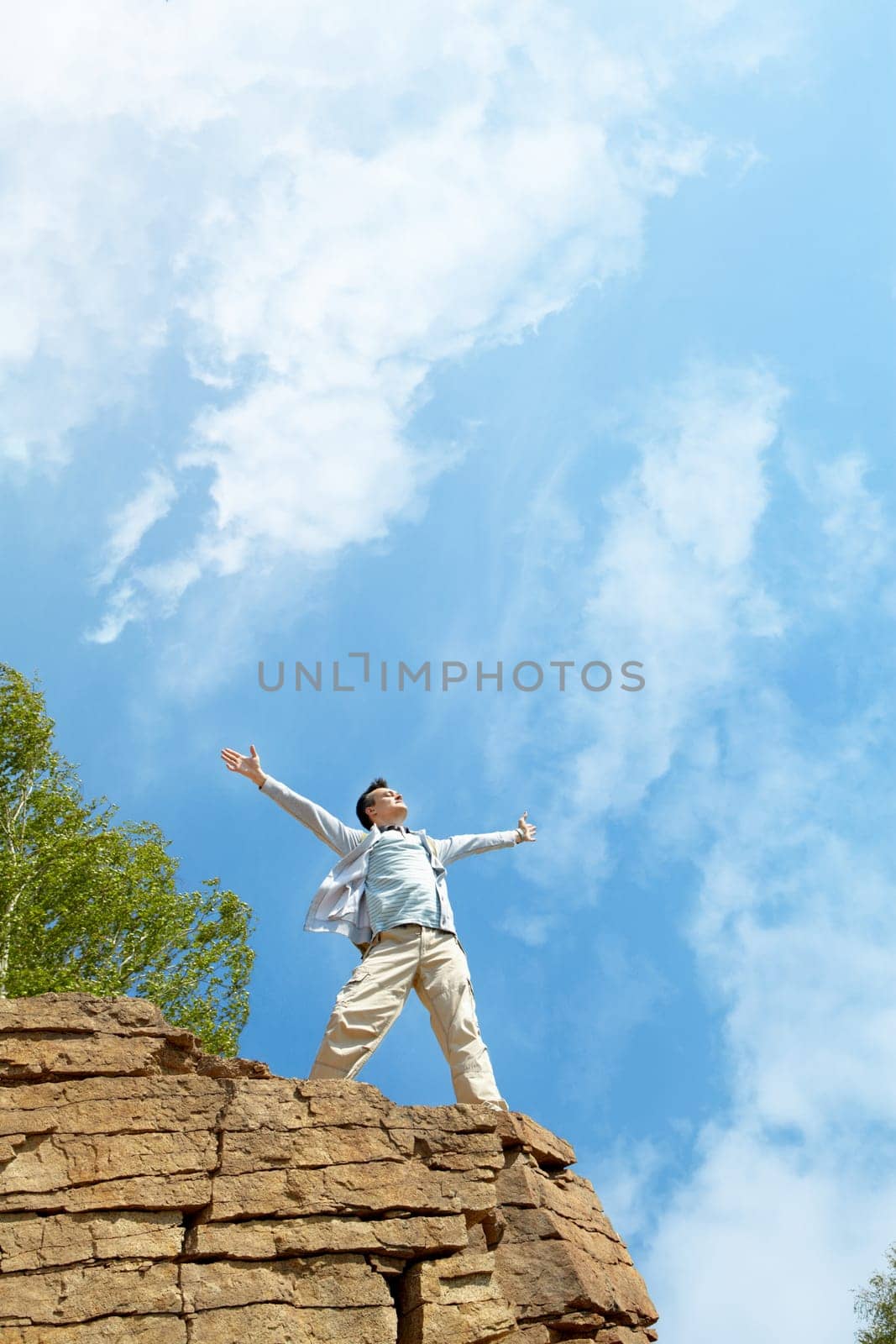 Portrait of free man standing on cliff with stretched arms and enjoying hot day