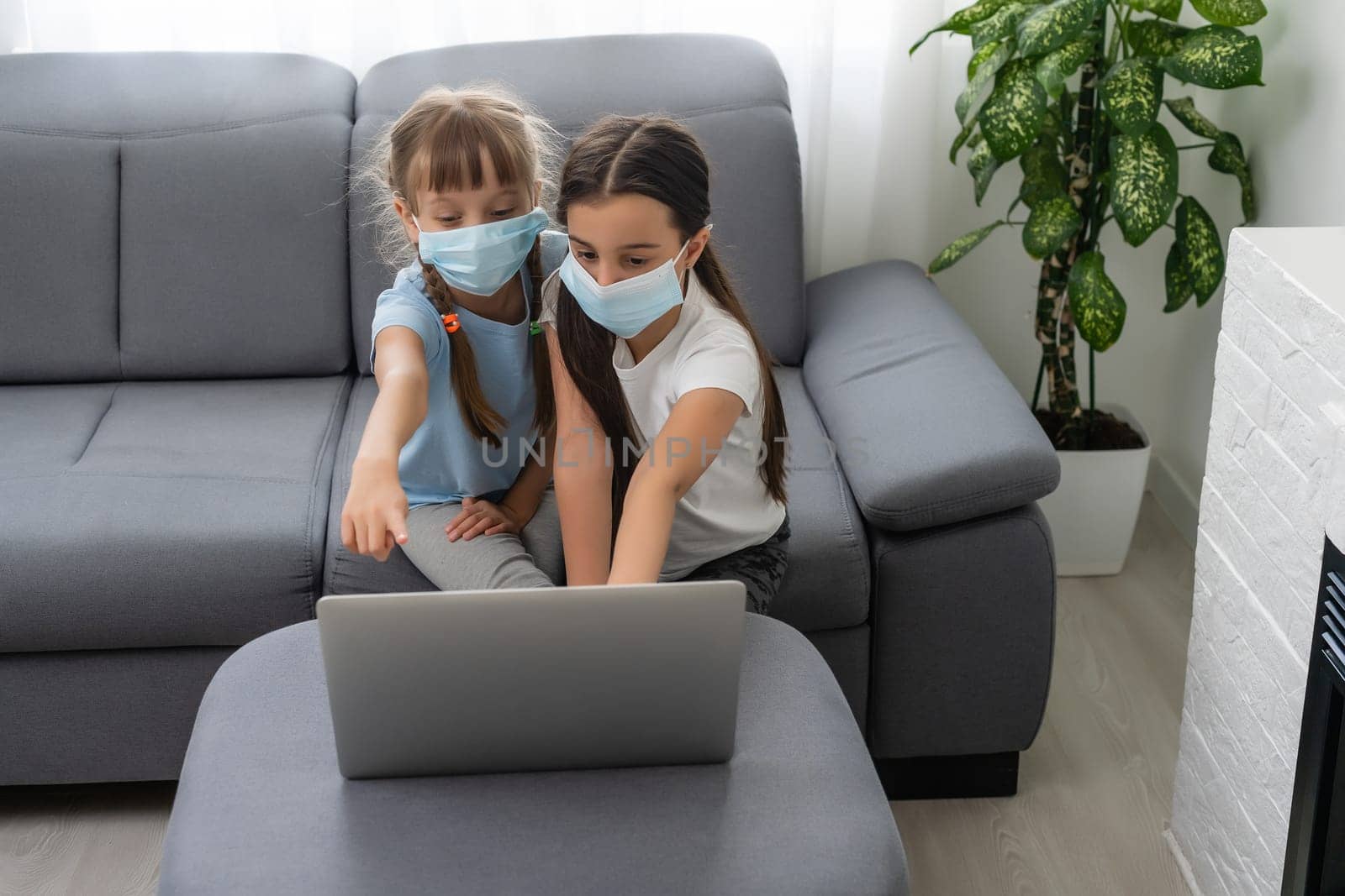 Young elementary school girls with face protective mask watching online education class. Coronavirus or Covid-19 lockdown education concept. by Andelov13