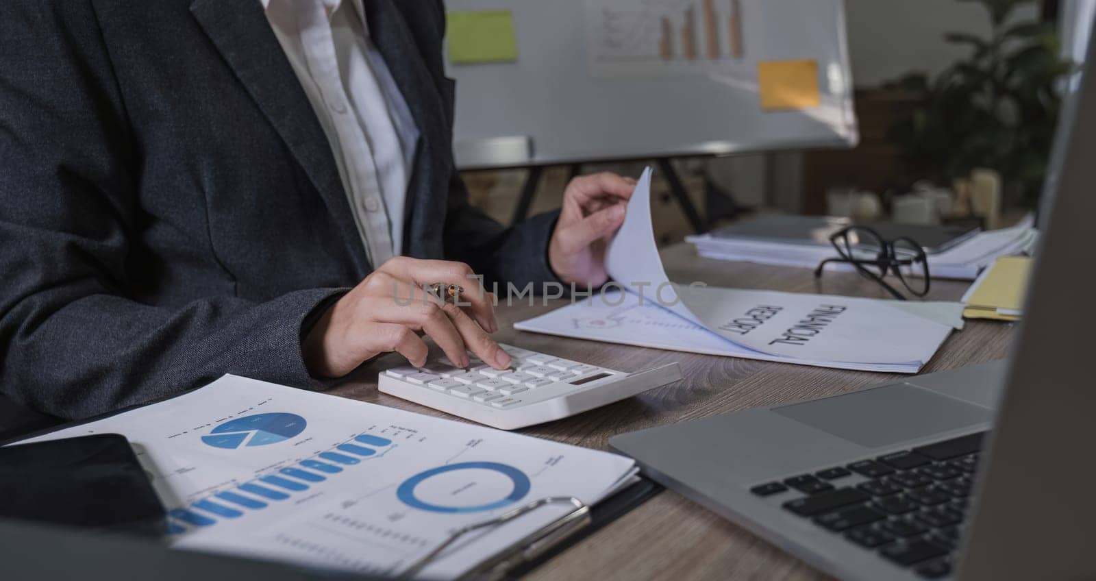 Close up Business woman using calculator and laptop for do math finance on wooden desk in office and business working background, tax, accounting, statistics and analytic research concept by wichayada