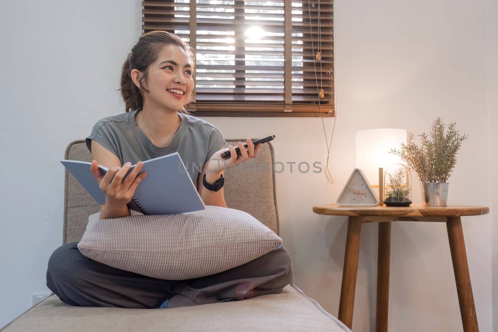 Happy young woman reading book on sofa at home. Lifestyle freelance relax and use smartphone in living room. Lifestyle Concept by wichayada