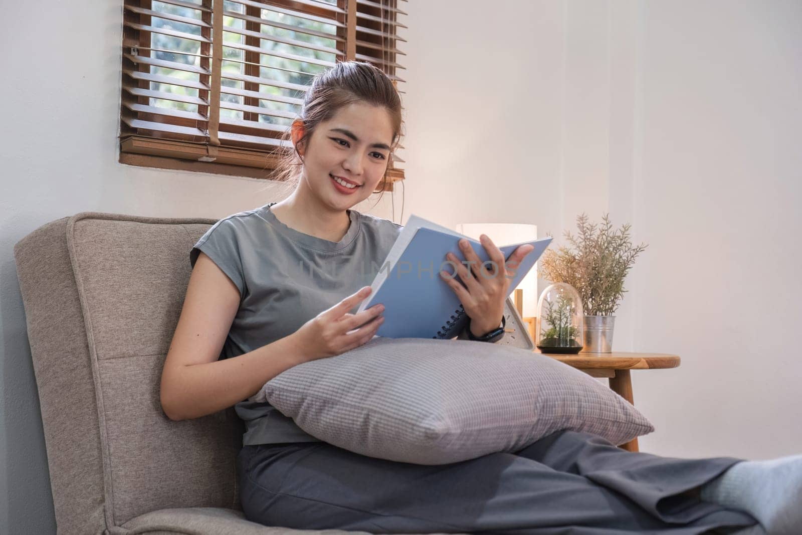 Happy young woman reading book on sofa at home. Lifestyle freelance relax in living room. Lifestyle Concept by wichayada