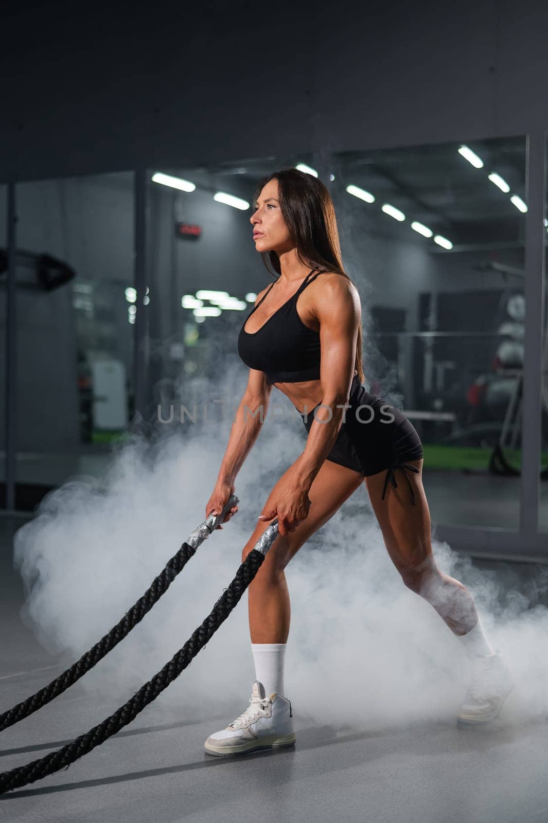 Caucasian woman doing exercise with ropes. Circuit training in the gym. Vertical photo. by mrwed54
