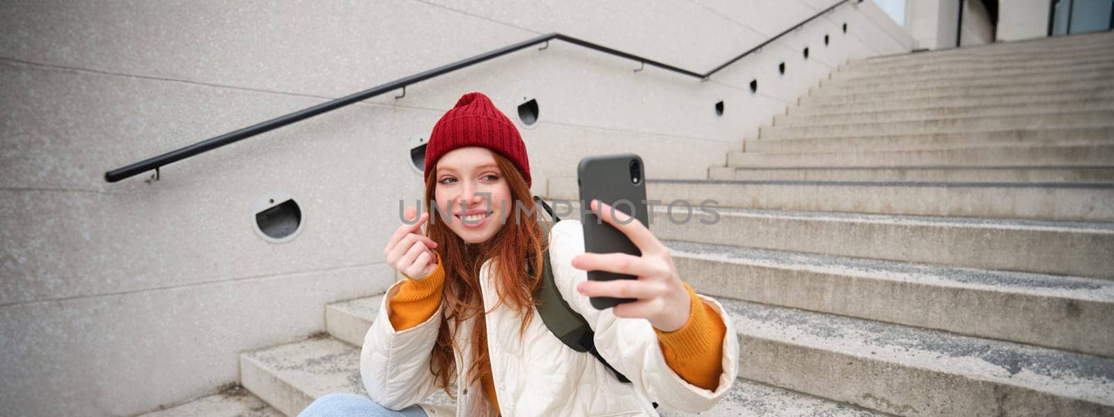 Urban girl takes selfie on street stairs, uses smartphone app to take photo of herself, poses for social media application.
