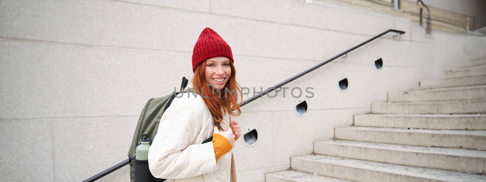 Happy young girl, redhead tourist in red hat with backpack, walks around town, explores city, backpacking around europe, travelling alone by Benzoix