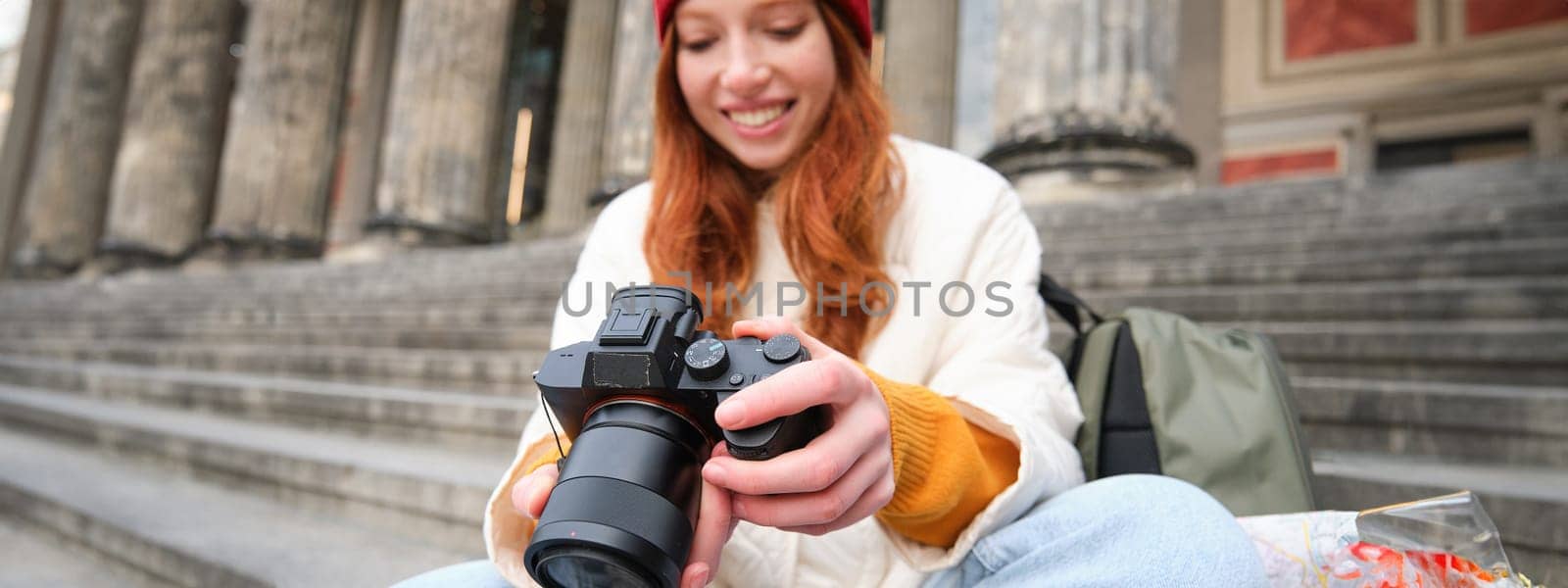Young student, photographer sits on street stairs and checks her shots on professional camera, taking photos outdoors by Benzoix
