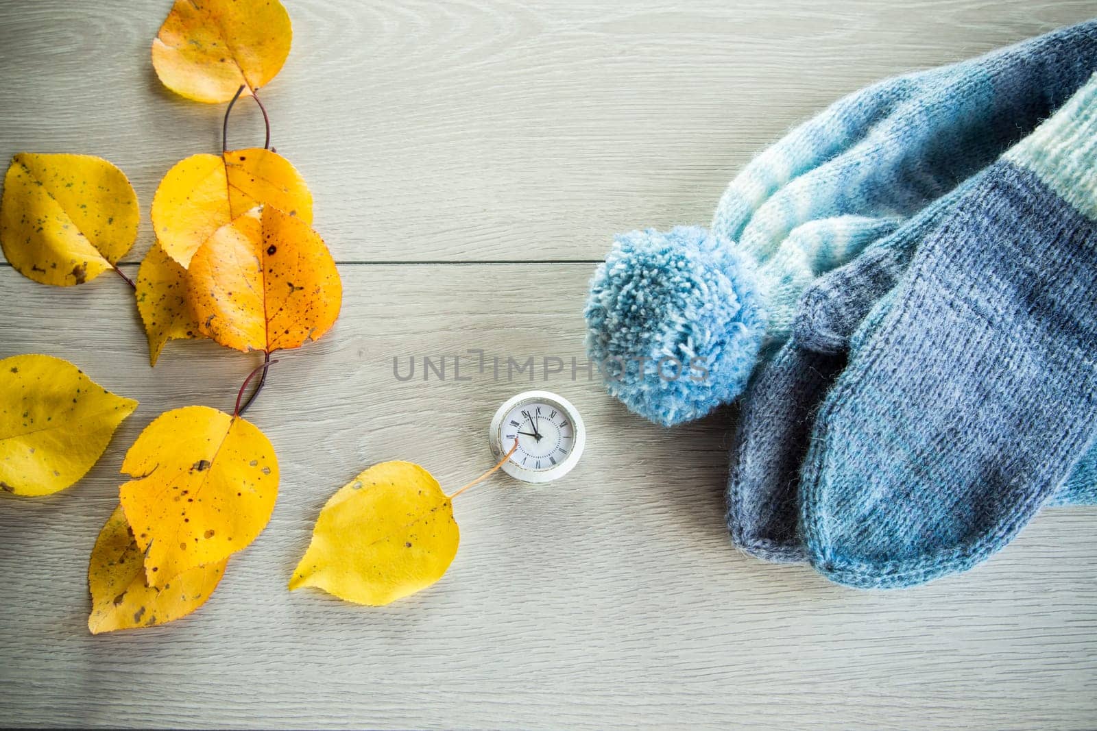 Autumn foliage, winter mittens and a clock on a wooden table. Change to winter time.