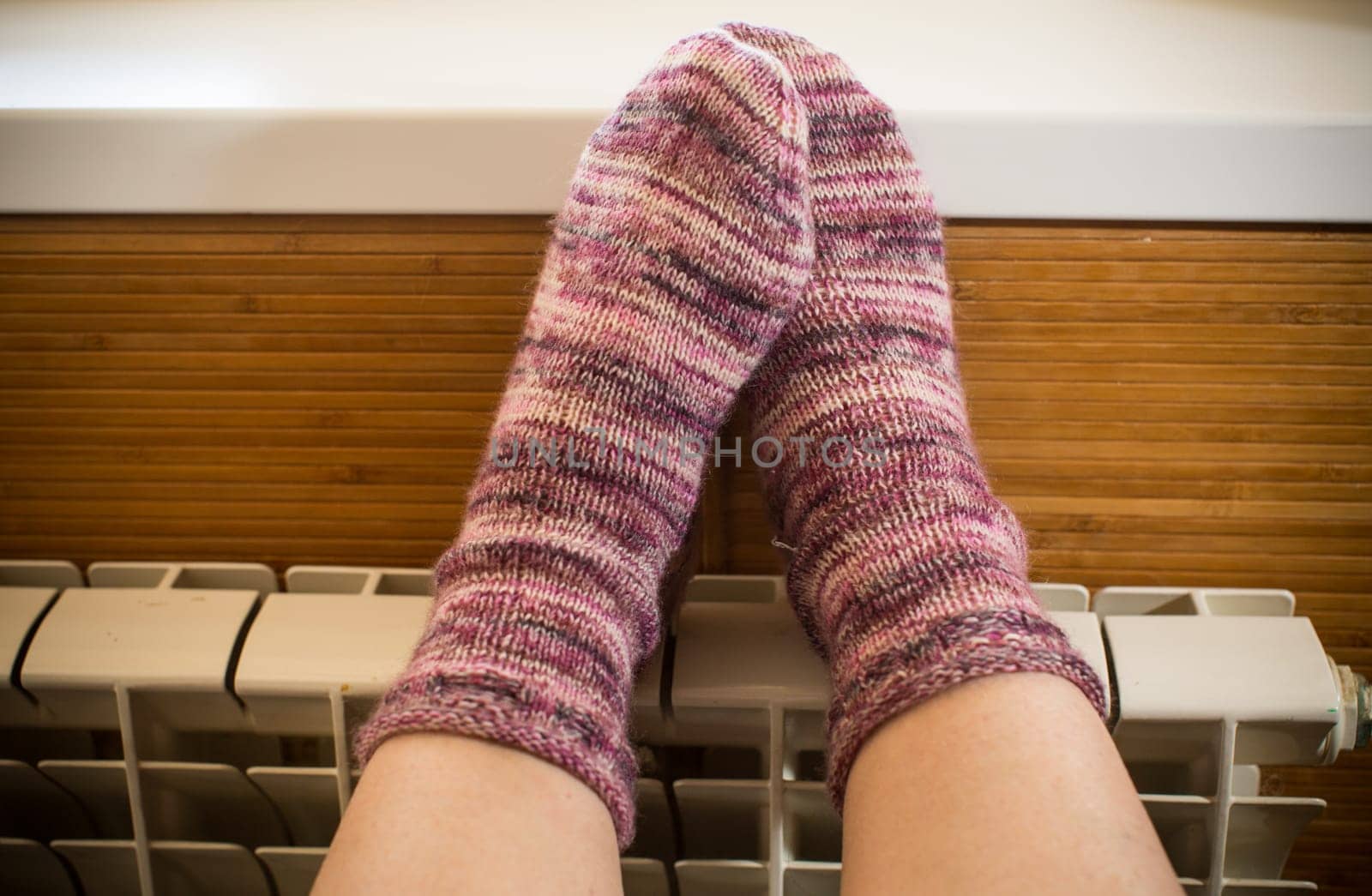 Feet in warm winter socks warm up on the radiator. by Rawlik