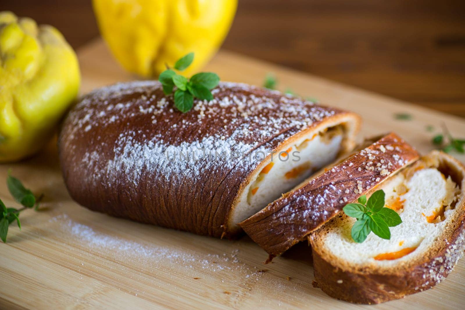 Cooked sweet pie with quince and pumpkin inside, yeast dough roll, on a wooden table.