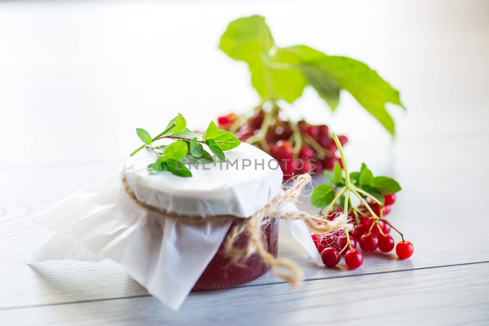 viburnum jam in a glass jar and fresh red viburnum on a light wooden table.