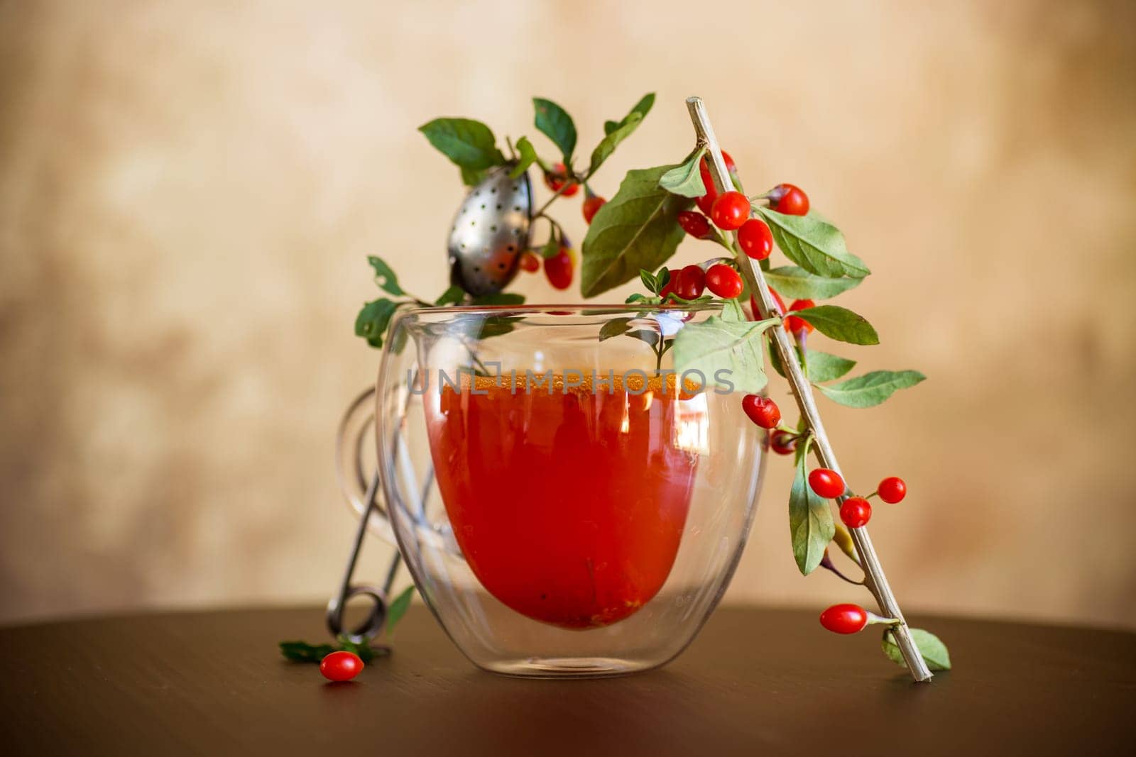 Prepared hot drink from ripe goji berries in a glass cup on a wooden table.
