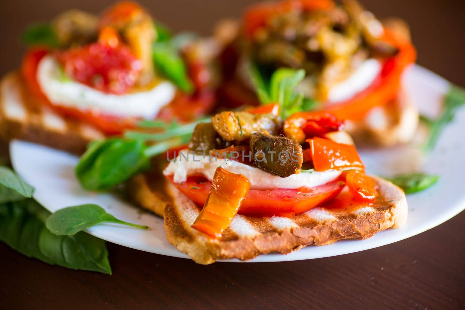 Prepared sandwich with tomatoes, mozzarella and fried eggplant with mushrooms in a plate on a wooden table.