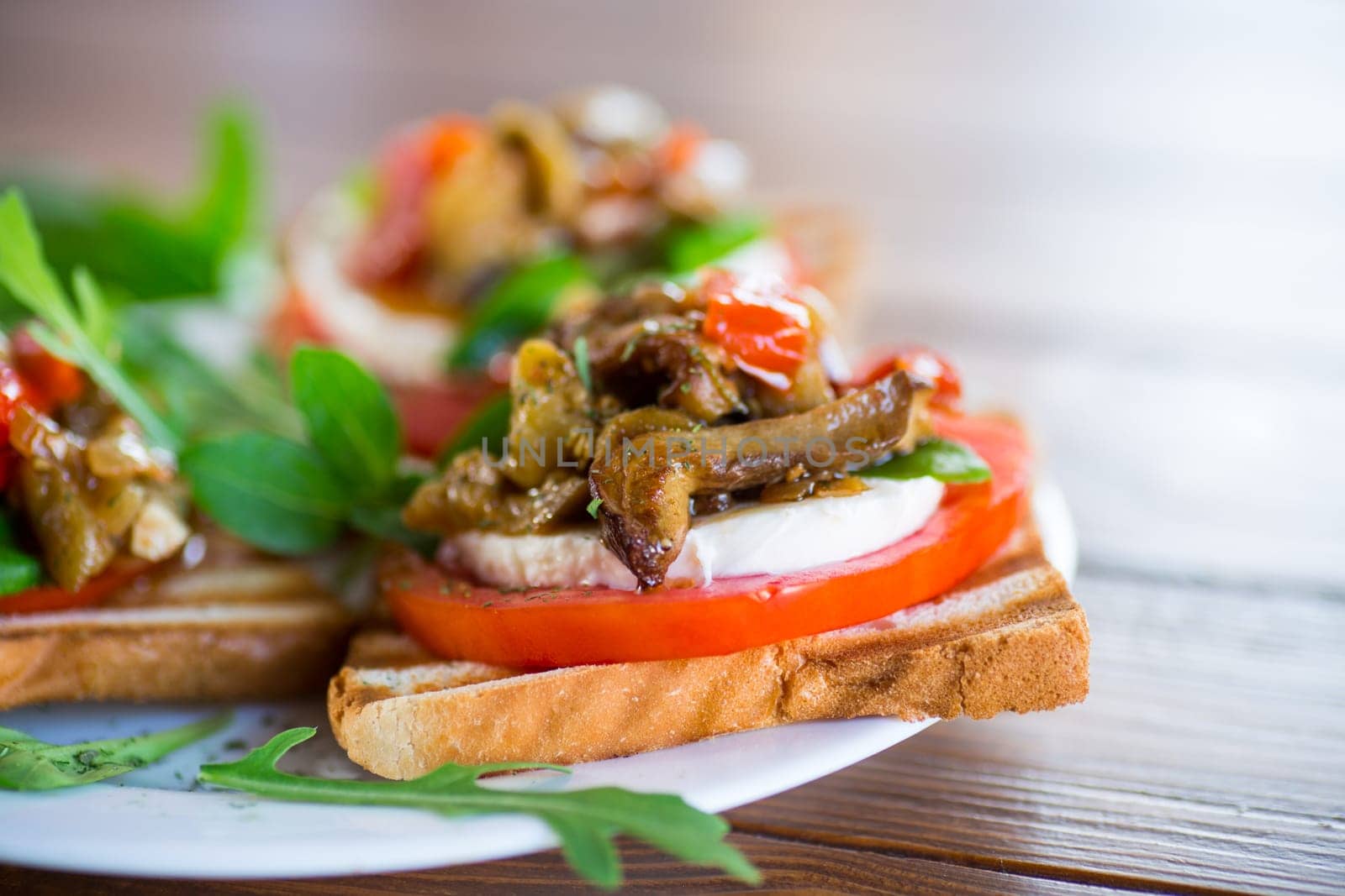 Prepared sandwich with tomatoes, mozzarella and fried eggplant with mushrooms in a plate on a wooden table.