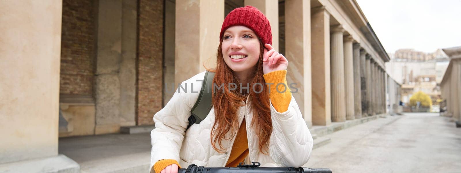 Young smiling redhead girl, student rides electric scooter, rents it and travels around city by Benzoix
