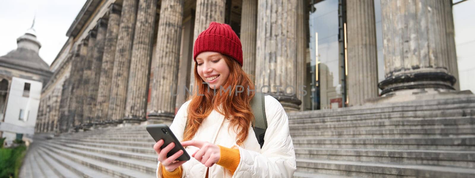 Portrait of young urban girl with backpack, using smartphone, walking around city, looking at map on mobile app, checking direction.