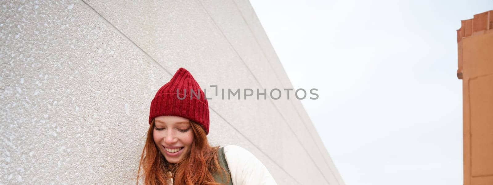 Joyful girl tourist looks at mobile phone, texts message on smartphone social media application, walks around city, looks for sightseeing on mobile app.