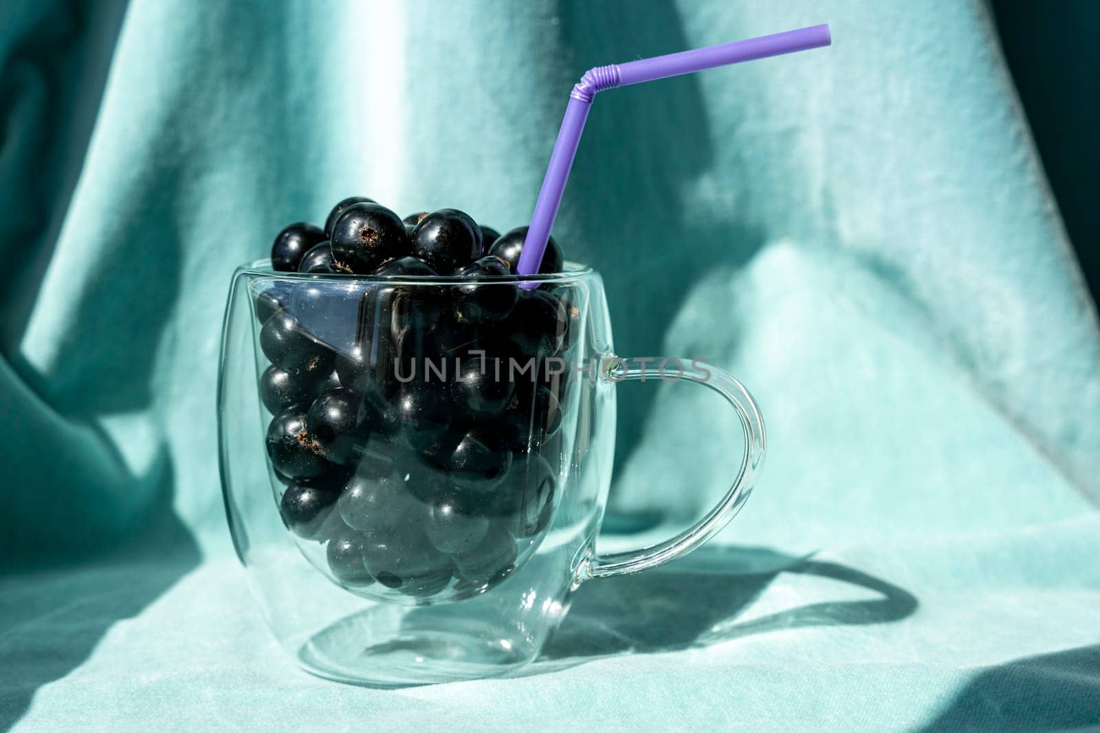 Summer fresh black currant berries in a glass mug with a cocktail tube by audiznam2609