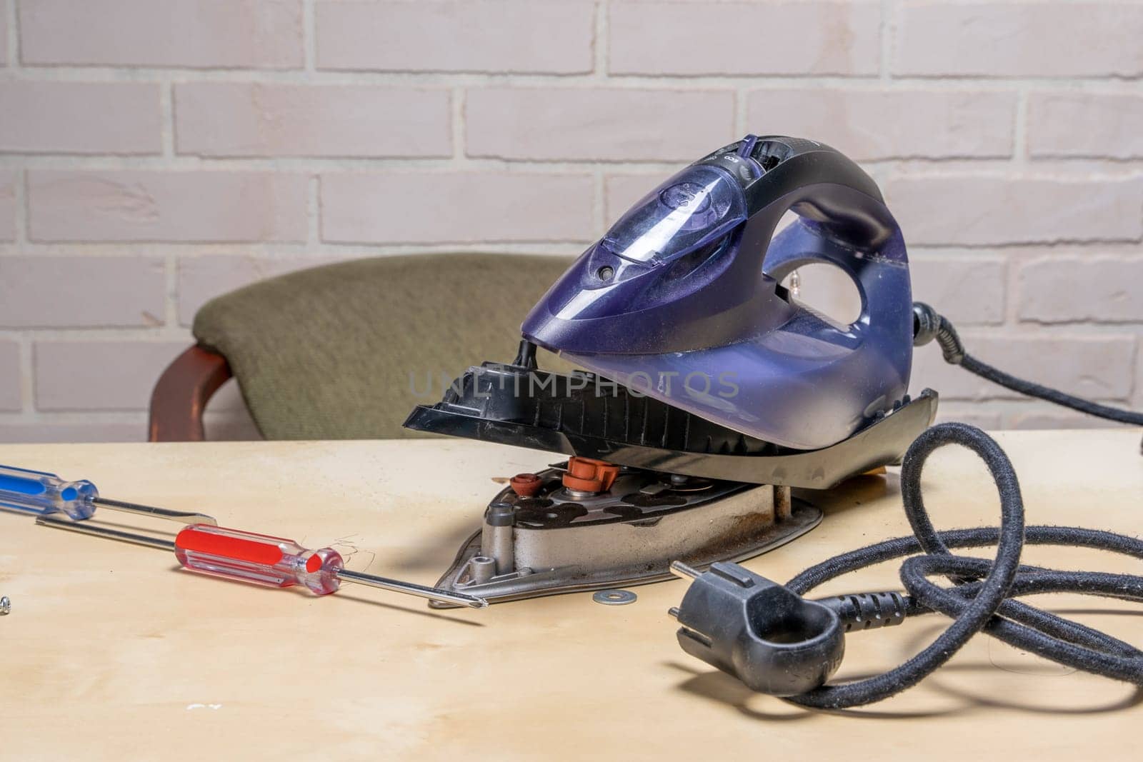 Disassembled electric iron. repairman checking and fixing broken iron. repairman checking and fixing broken steam ironusing simple tools. closeup