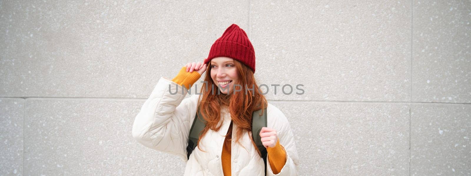 Young stylish girl traveller goes sightseeing, travels around city with backpack, tourist smiles and looks around. Copy space