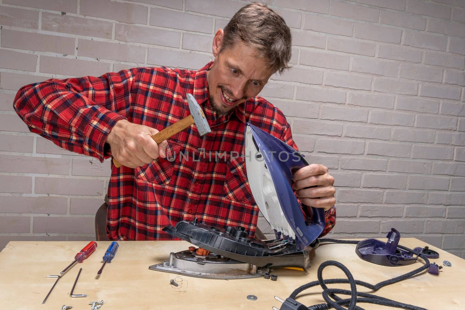 a funny and annoyed grief-stricken master repairs an electric iron. the master repairs the iron in the workshop on the table using tools. Disassembled electric iron.