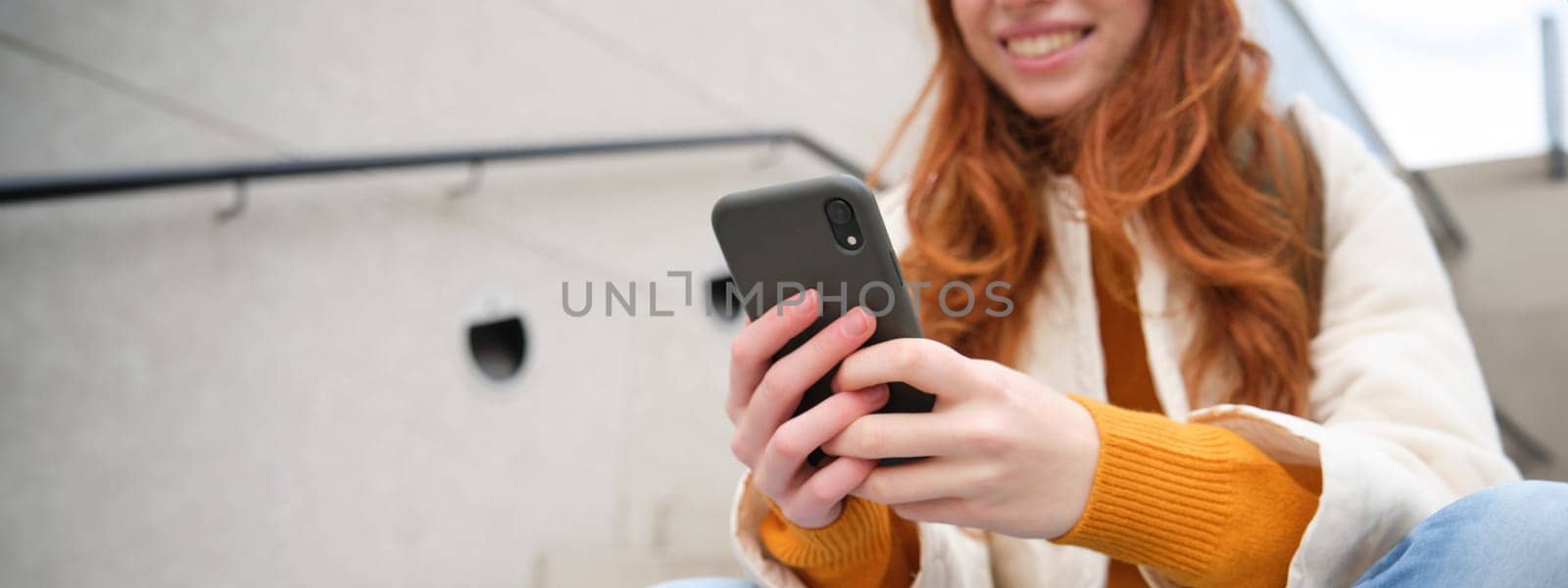 Close up portrait of girls hands holding smartphone. Woman sits on stairs on street and uses mobile phone, chats, reads message or uses application.