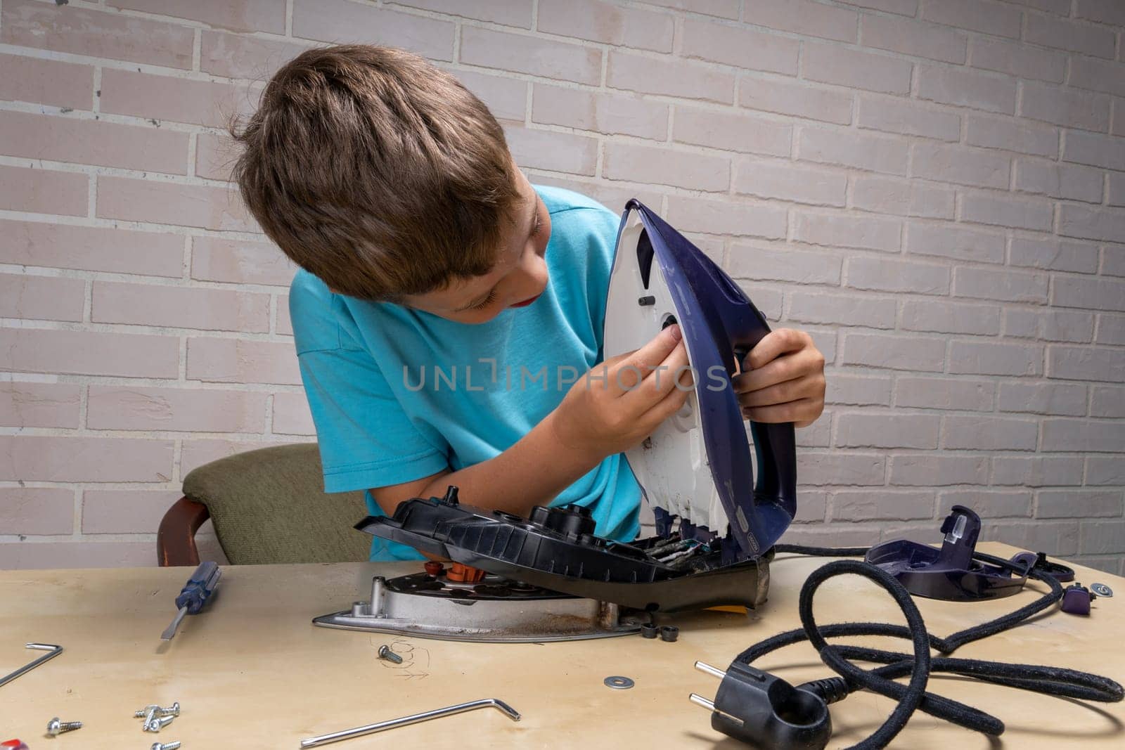 boy helps his mother. a funny master repairs an electric iron on the table using tools. Disassembled electric iron.