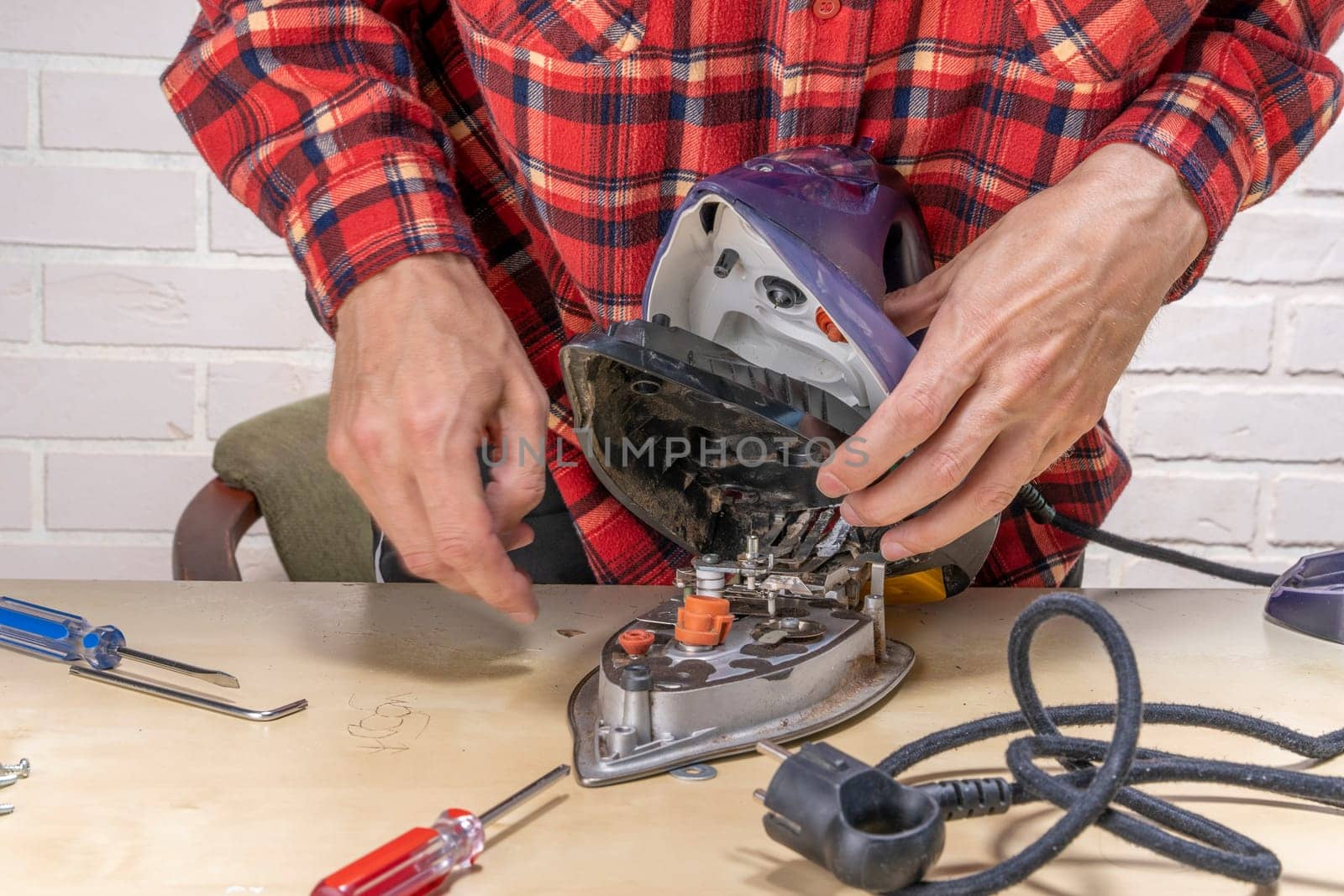 husband or the head of the family is trying to repair a broken steam iron at home on the table using simple tools. Disassembled electric iron. repairman checking and fixing broken iron