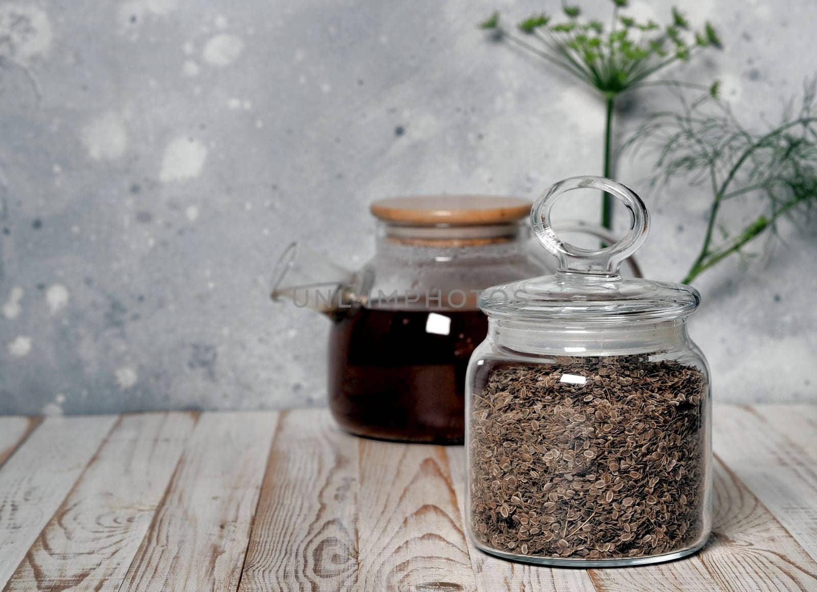 Dried seeds in a glass jar on the background of a teapot with tea on a natural wooden table. The concept of dried healthy herbs. by TatianaPink