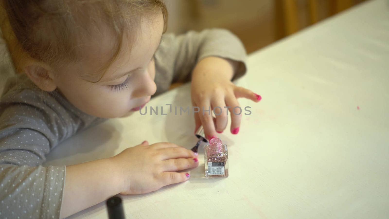 A little girl paints her nails with pink polish. The girl paints her nails like an adult. 4k